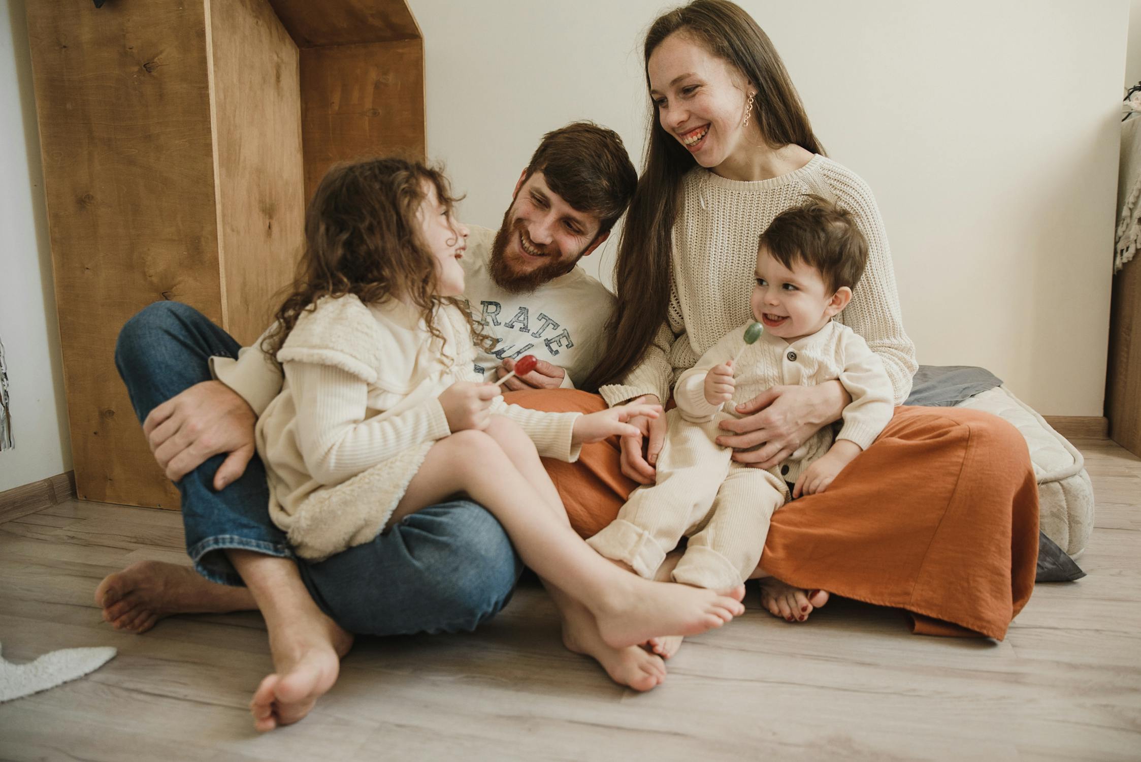 Young couple sitting on the floor at home laughing with their toddler and baby, capturing the everyday family moments that motivate couples to discuss life insurance planning together