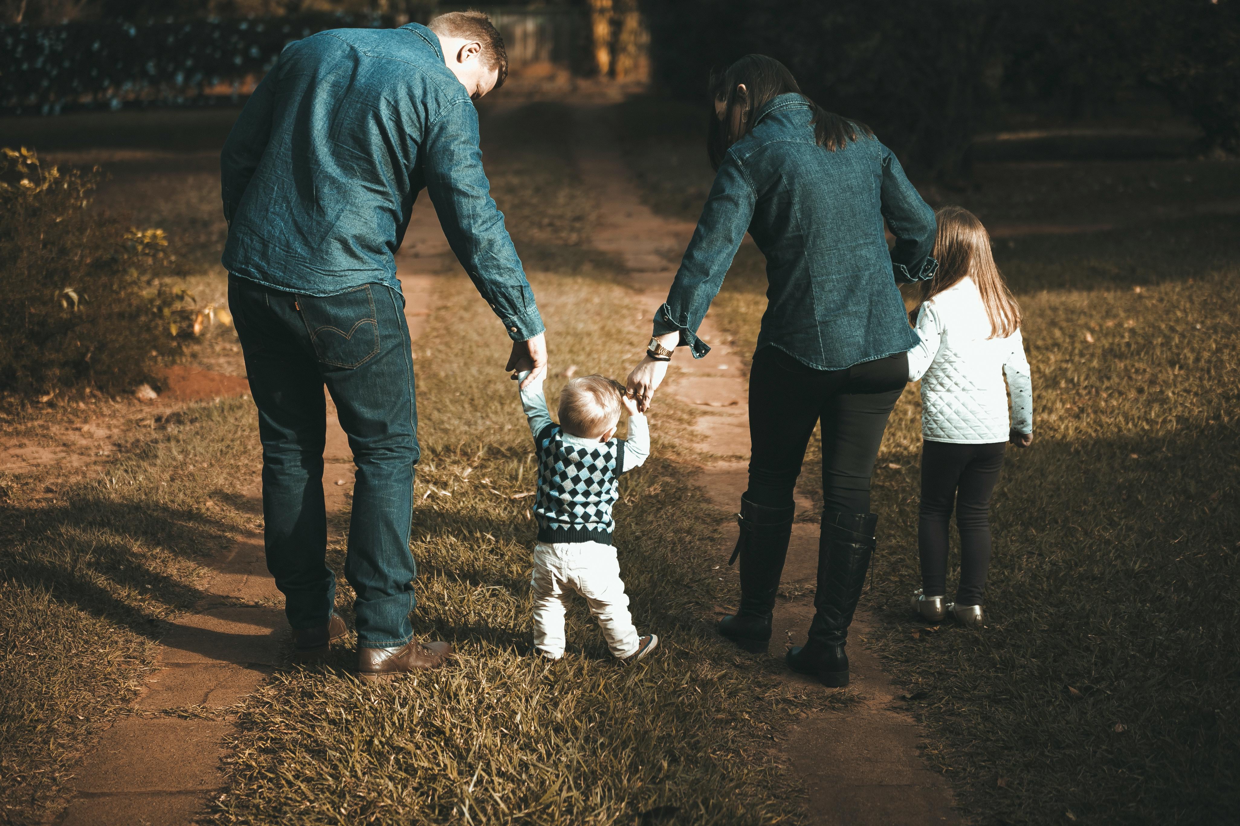 Parents helping toddler learn to walk outdoors